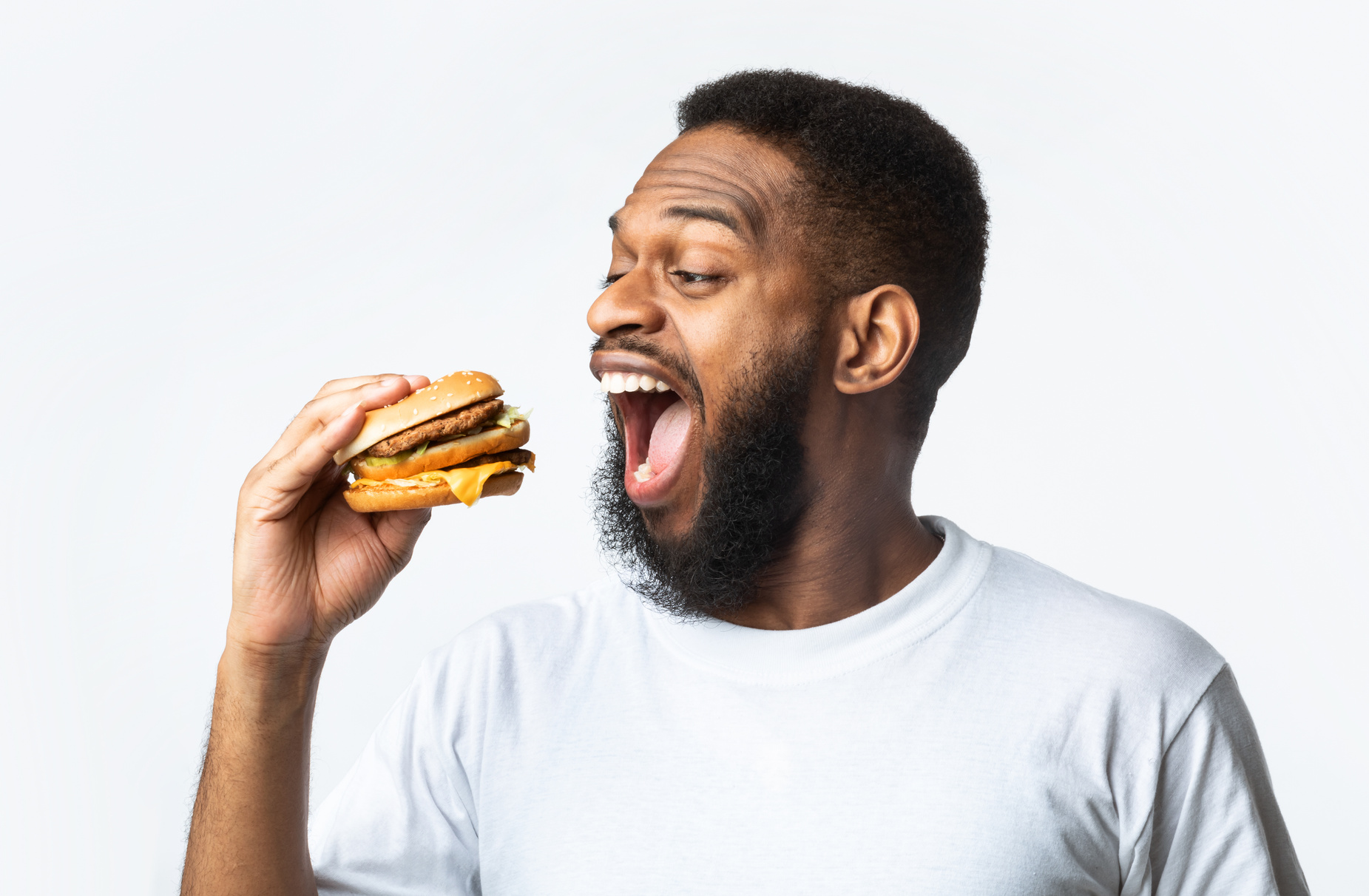 Hungry African American Guy Eating Burger Standing Over White Background